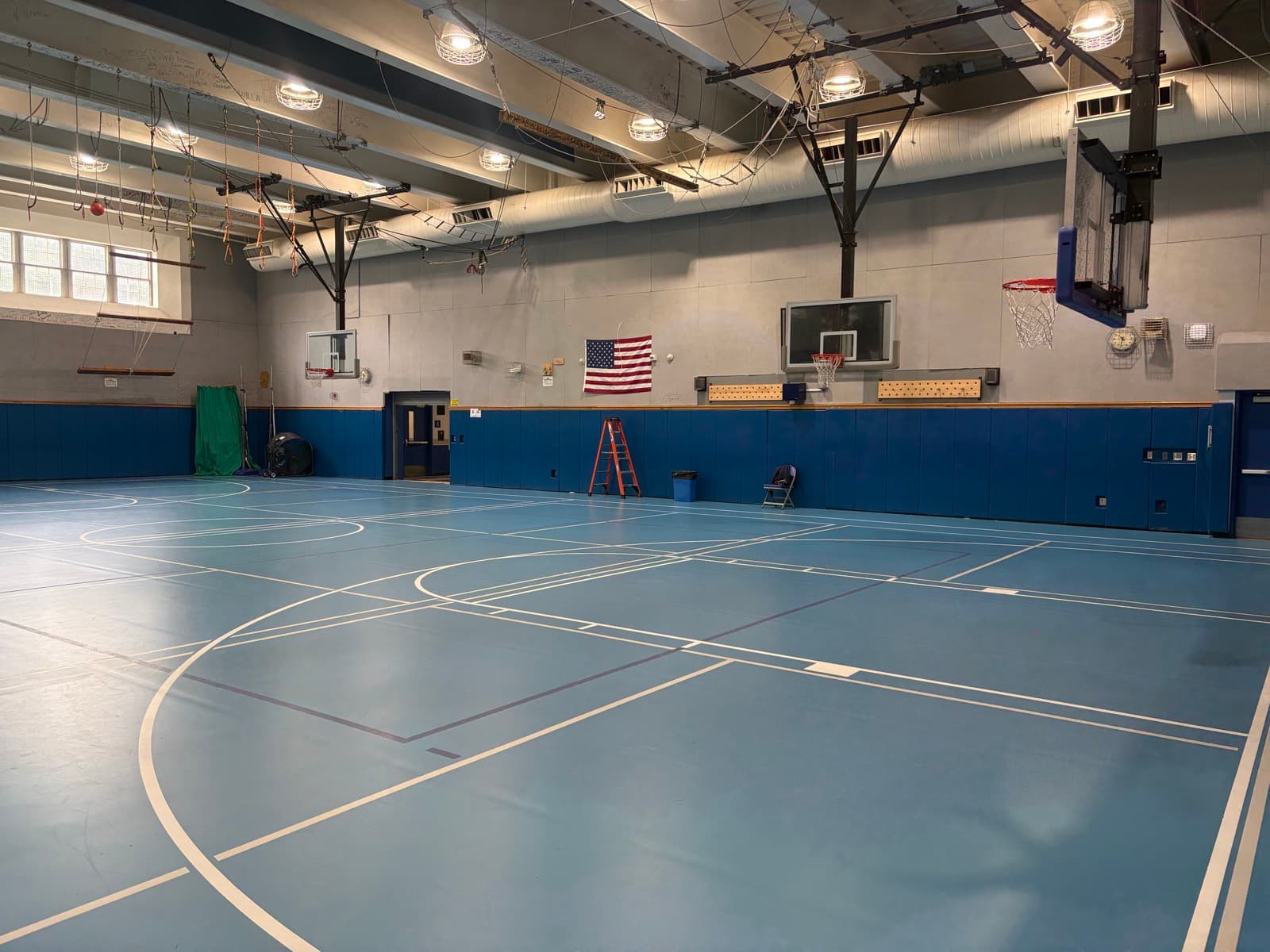 A Bronxville School gym with a blue court, wall padding, and basketball hoops