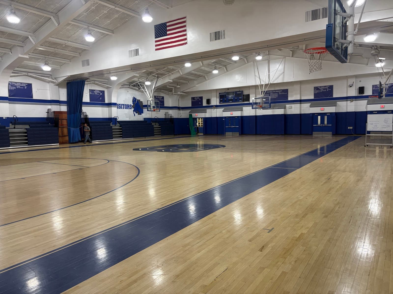 The Bronxville School main gym with the blue Bronco logo at center court, bleachers, and championship banners
